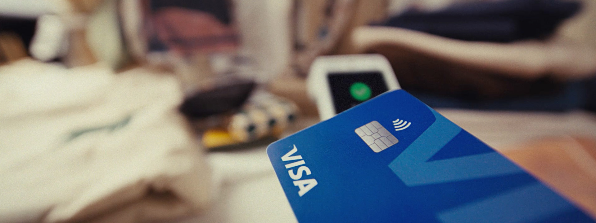 Close-up of a blue Visa contactless credit card being tapped on a payment terminal.