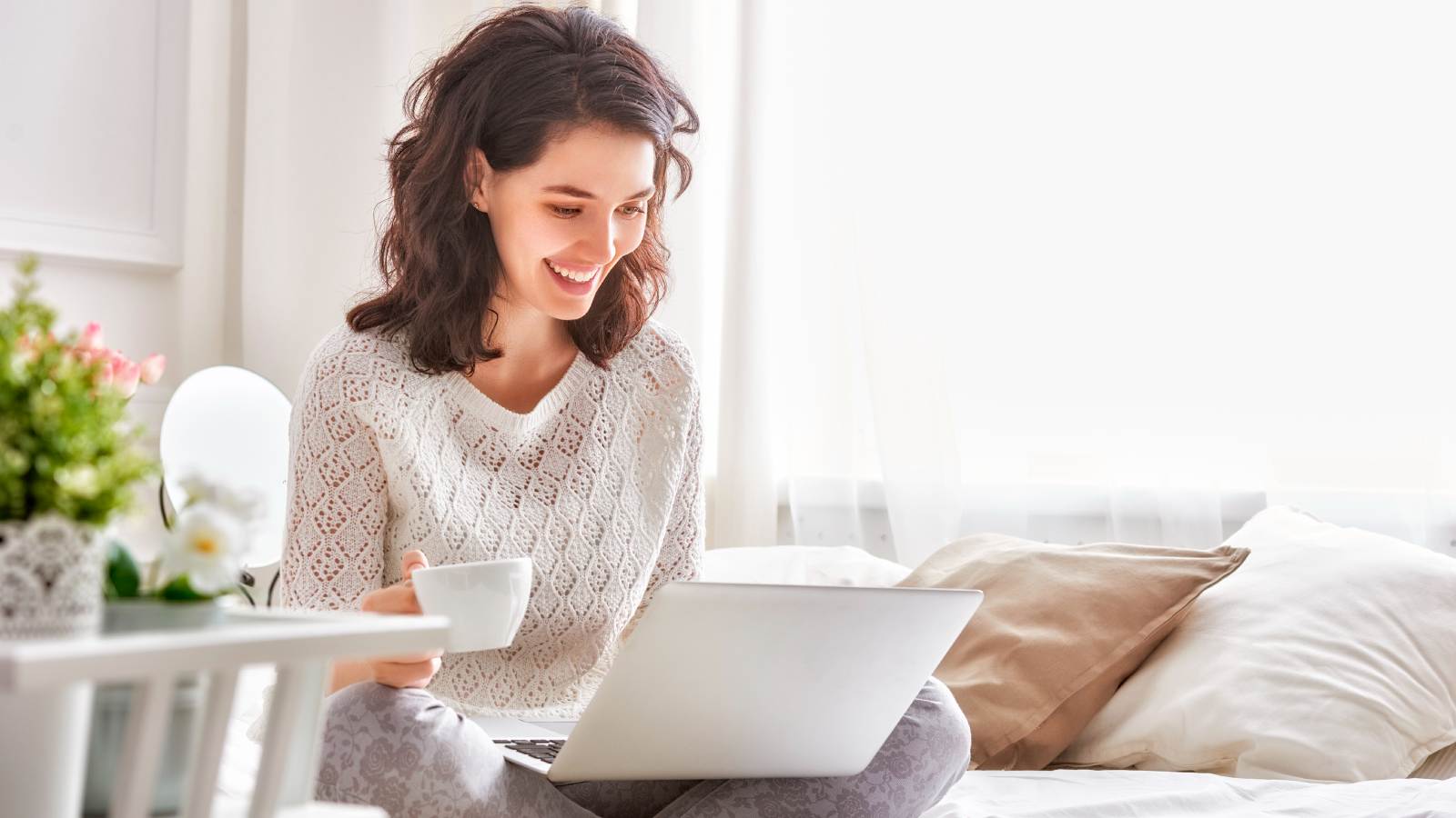 Woman on bed with coffee and laptop