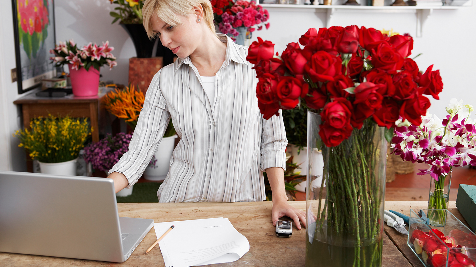 florist-laptop-1600x900 A woman standing at a table inside a flower shop, looking at her laptop.