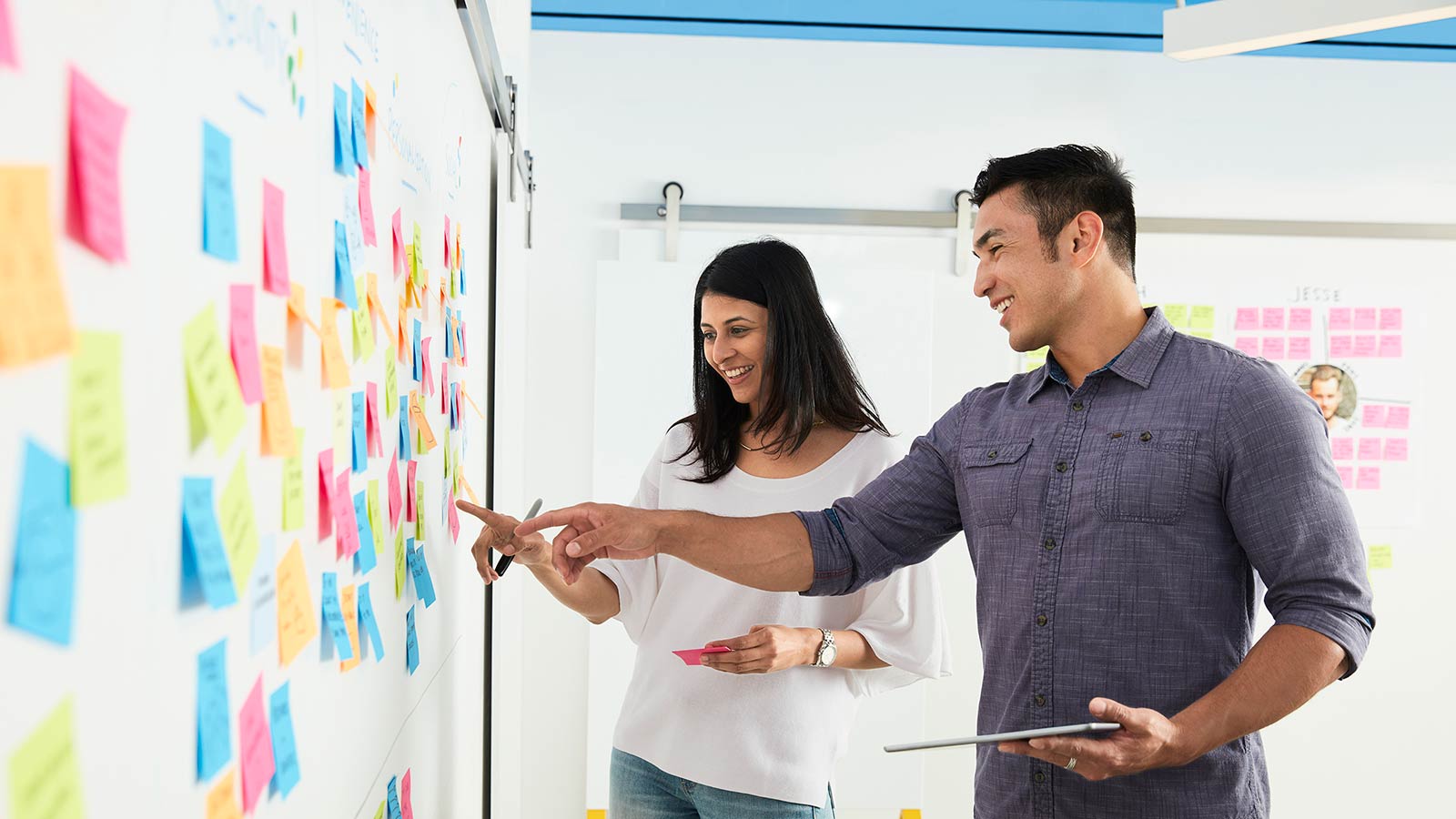 Man and woman in front of whiteboard with sticky notes of innovative ideas.